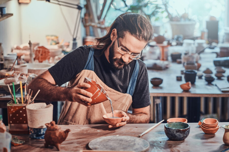 Diligent man is putting colourful clay to his new handmade pot.